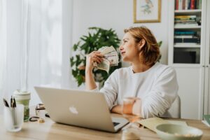 woman-sitting-and-holding-money-with-laptop-on-desk